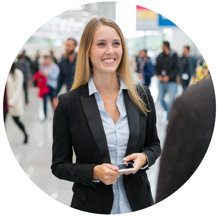 A young, smiling woman stands at a trade fair and talks to a visitor.
